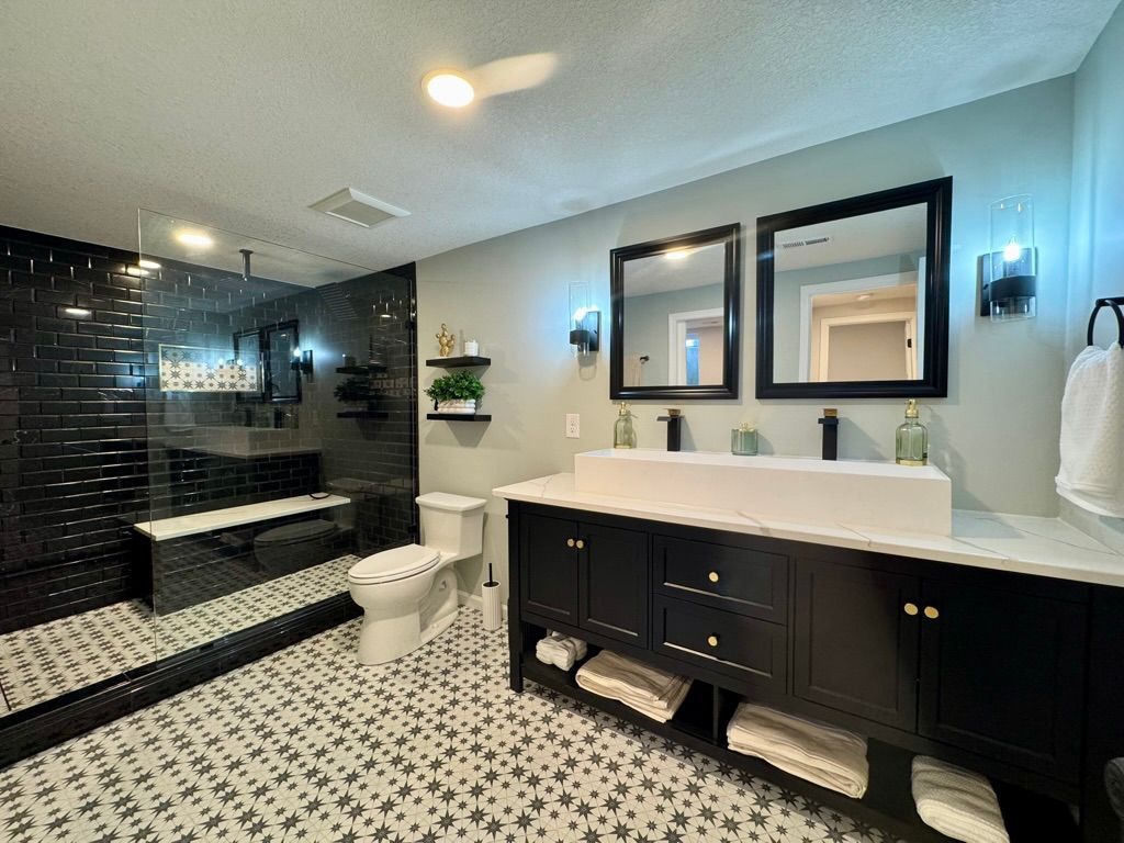 Modern bathroom with black vanity, white countertop, and patterned floor. Black tiled shower.