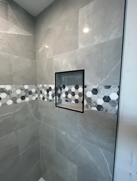 Gray tiled shower with a decorative mosaic band and built-in shelf.