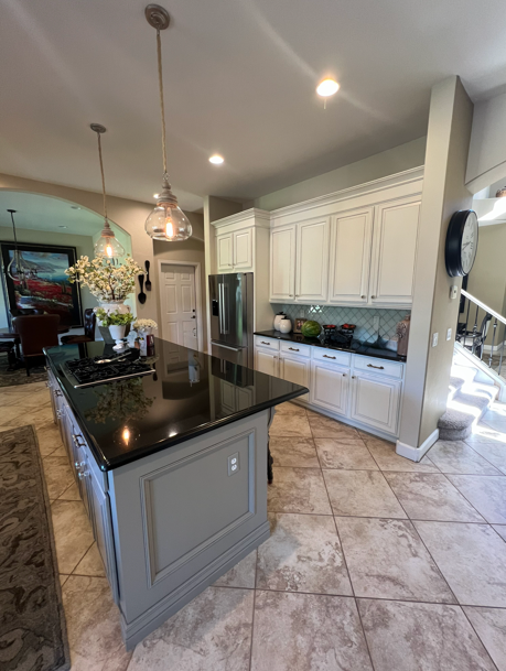 Kitchen with gray island and black countertop. White cabinets, stainless steel refrigerator, and tiled floor.