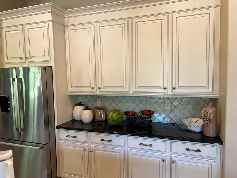 White kitchen cabinets with black countertop, stainless steel refrigerator.