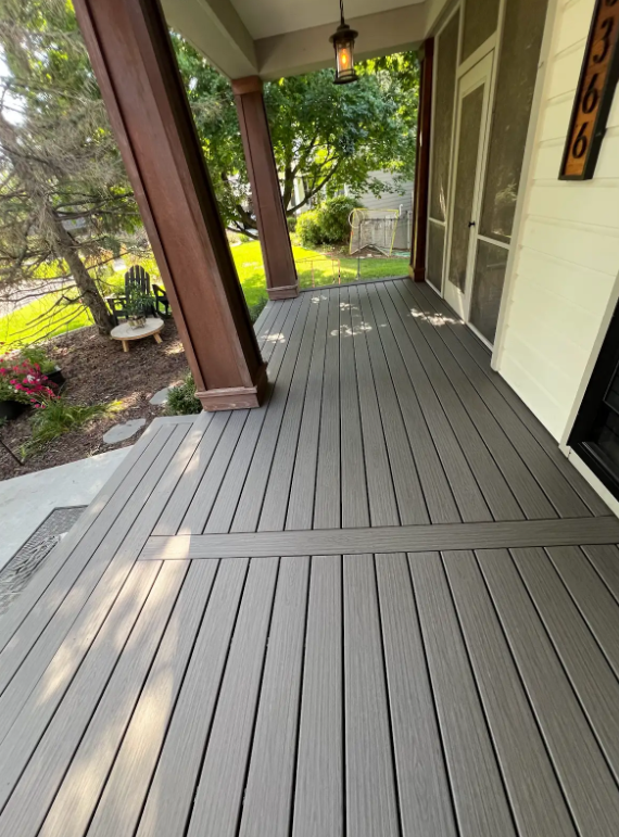 Gray composite deck of a porch. Brown support columns on left, white house wall on right.