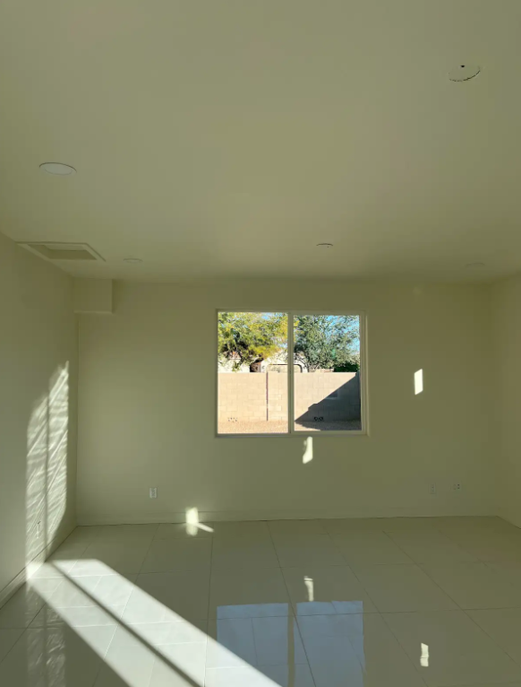 Empty room with window, sunlight and shadows on walls and floor.