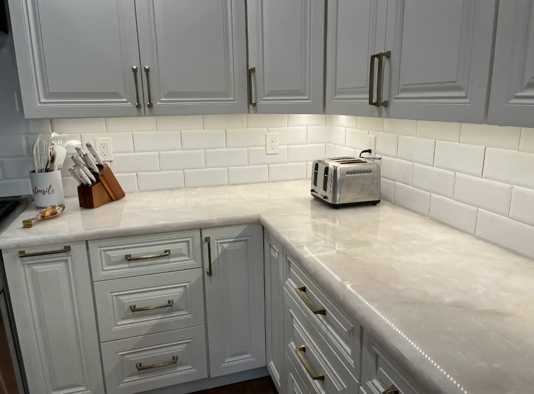 Gray and white kitchen cabinets with white countertops, subway tile backsplash, and a toaster.