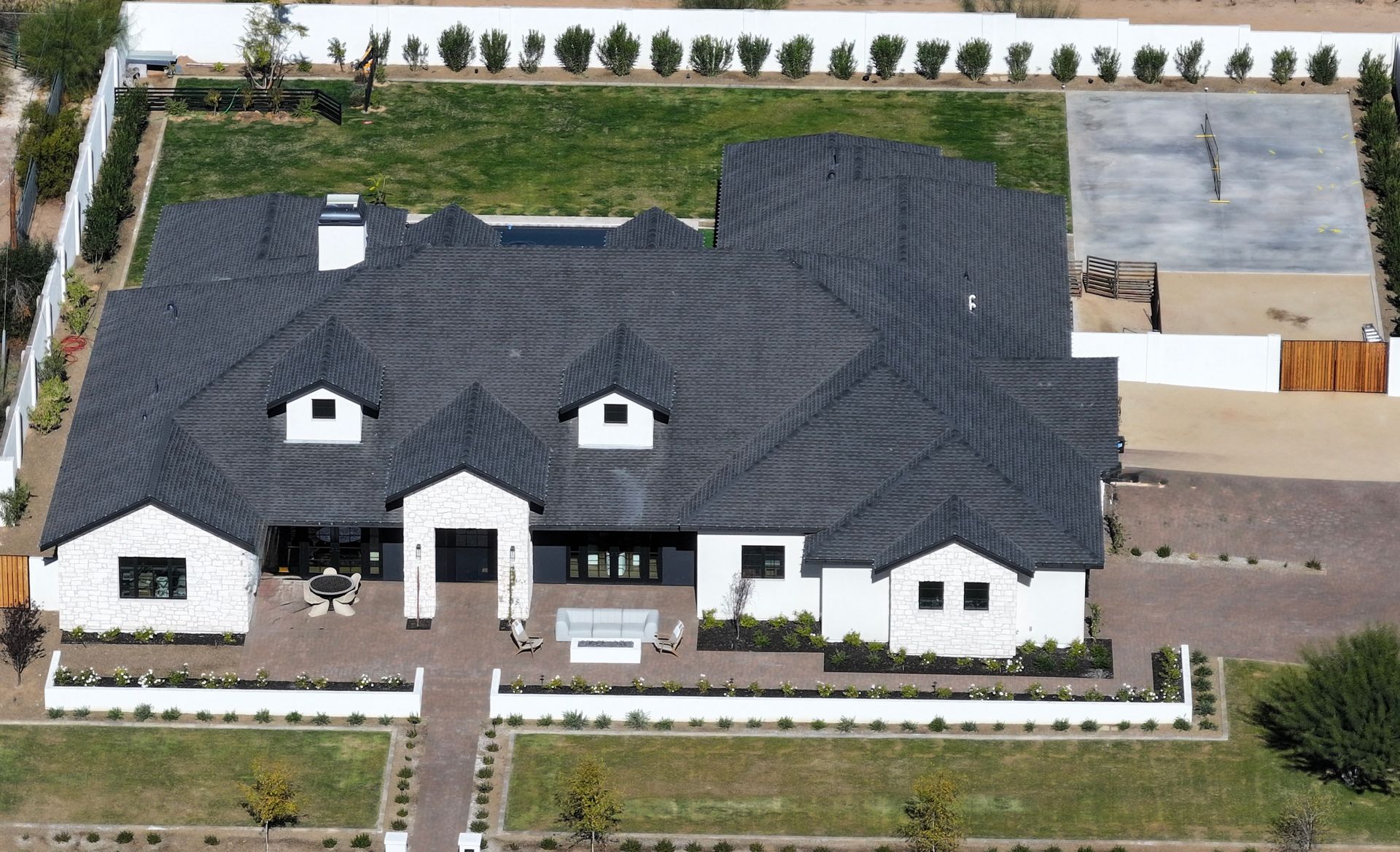 Aerial view of a large white house with a dark gray roof, tennis court, and a well-manicured lawn.