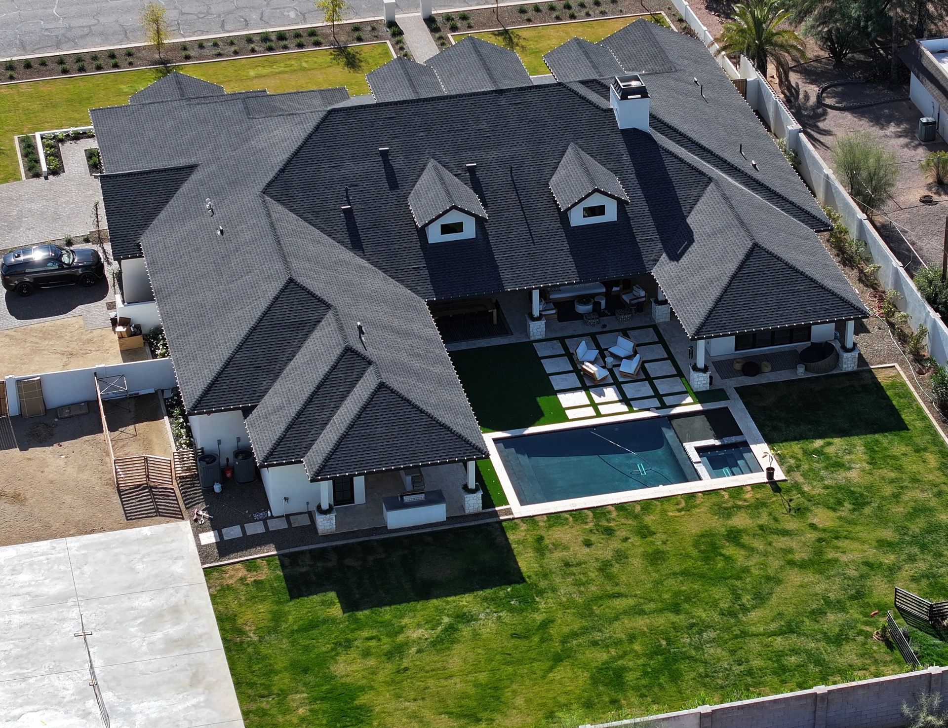 Aerial view of a large, modern home with a dark roof, pool, and green lawn.