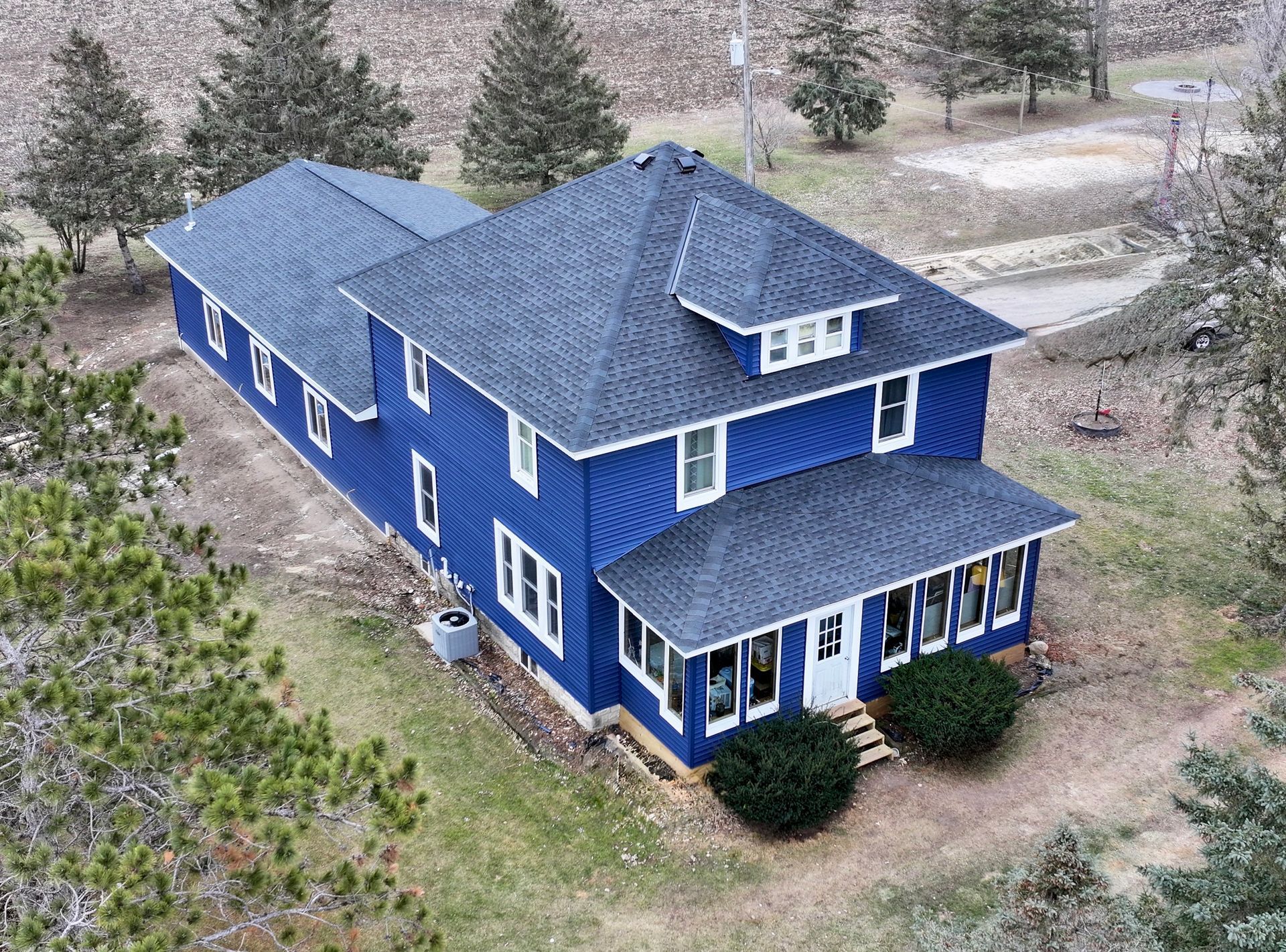 Blue two-story house with white trim and dark gray roof, surrounded by trees and grass.