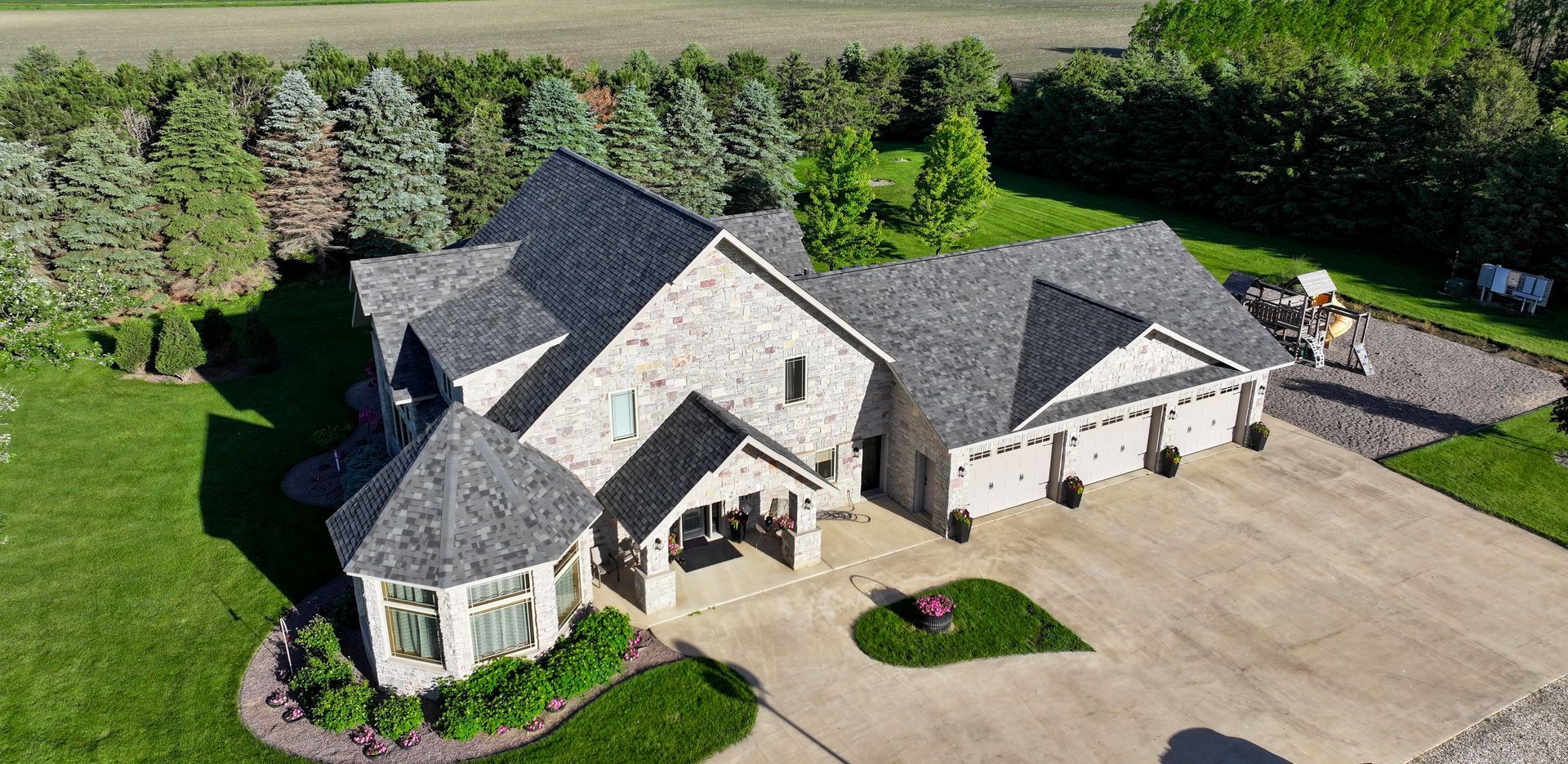 Aerial view of a large, gray-roofed house with a long driveway and green lawn.