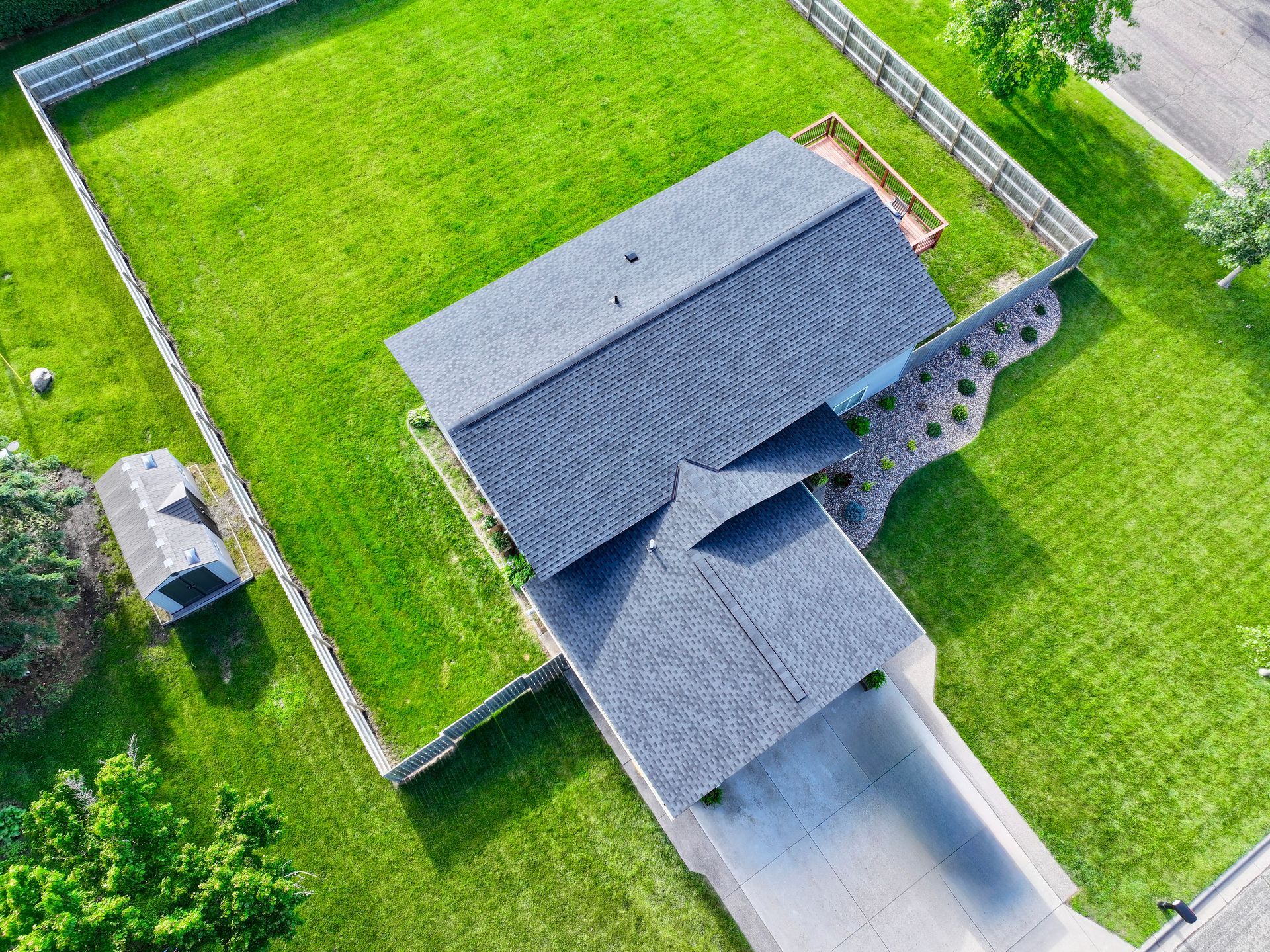 Aerial view of a house with a gray roof and a green lawn, surrounded by a fence.