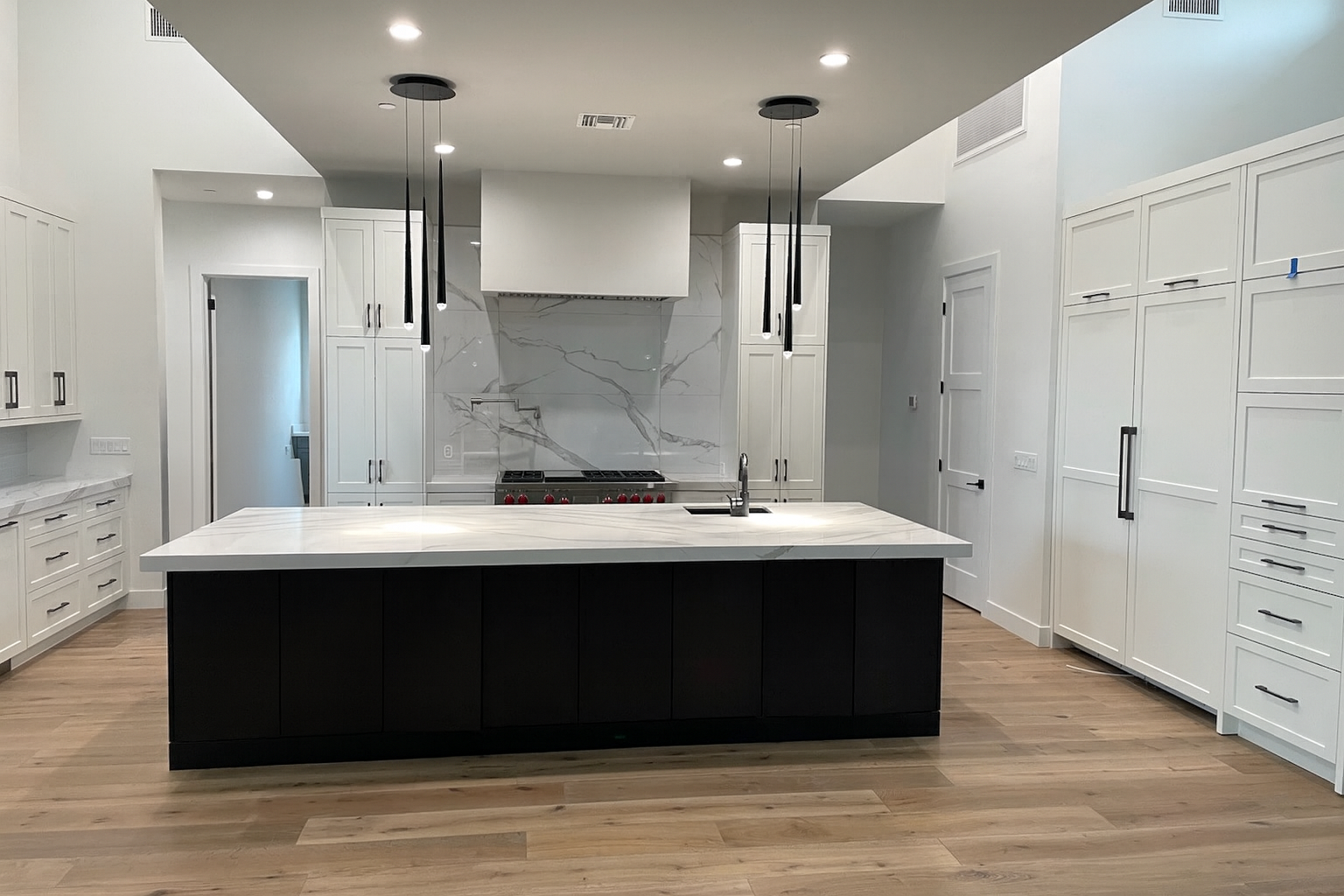 Modern kitchen with white cabinets, dark island, marble backsplash, and wooden floor.