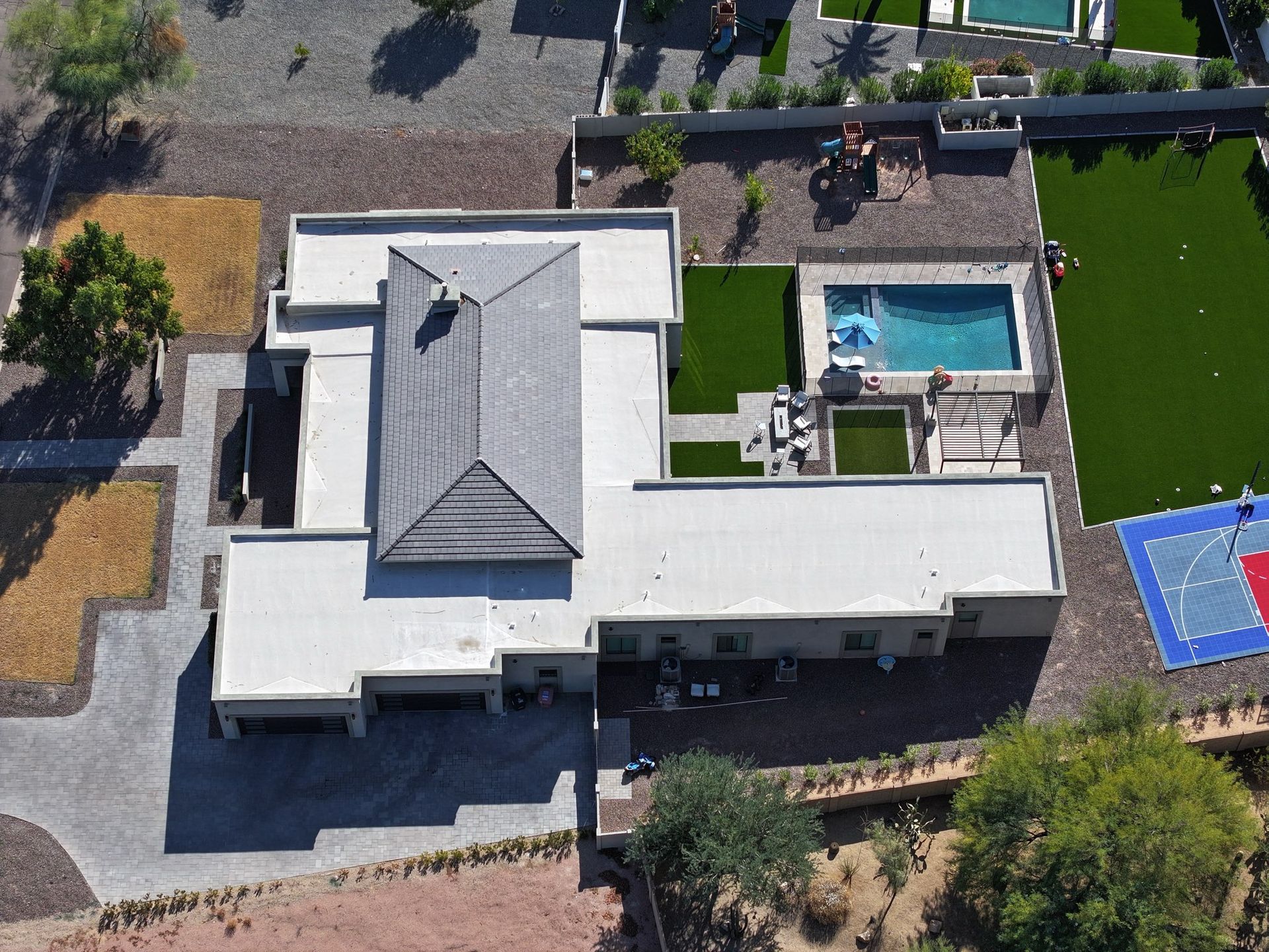 Aerial view of a modern house with a pool, patio, and sports court on a brown landscape.