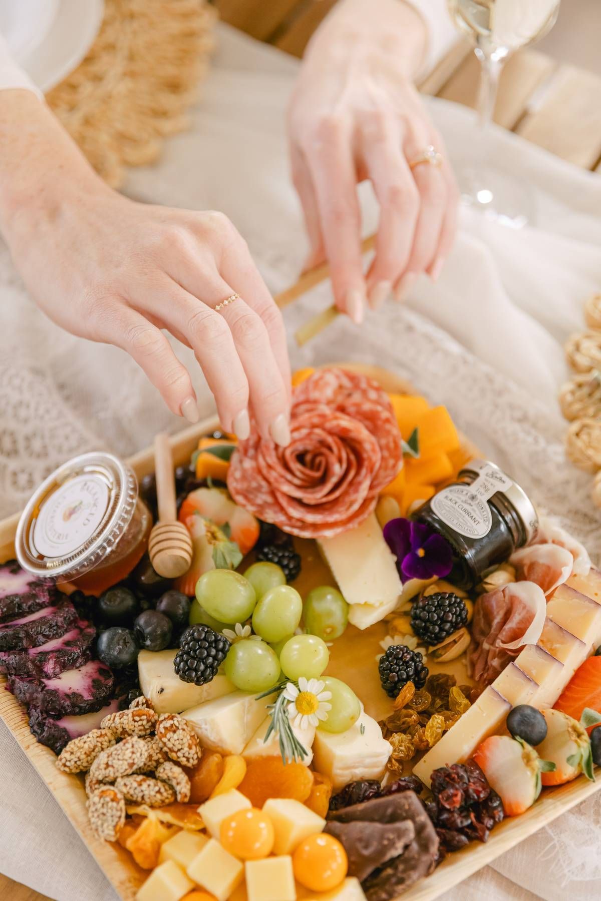 Hands arranging a charcuterie board with cheese, fruit, and meat on a wooden surface.
