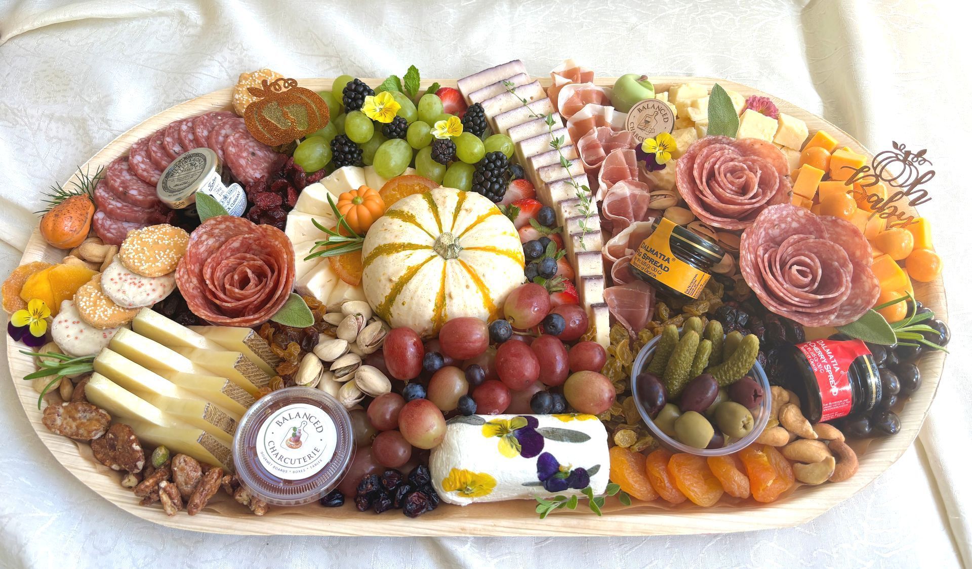 Oval charcuterie board with cheese, meats, fruits, nuts, and olives.