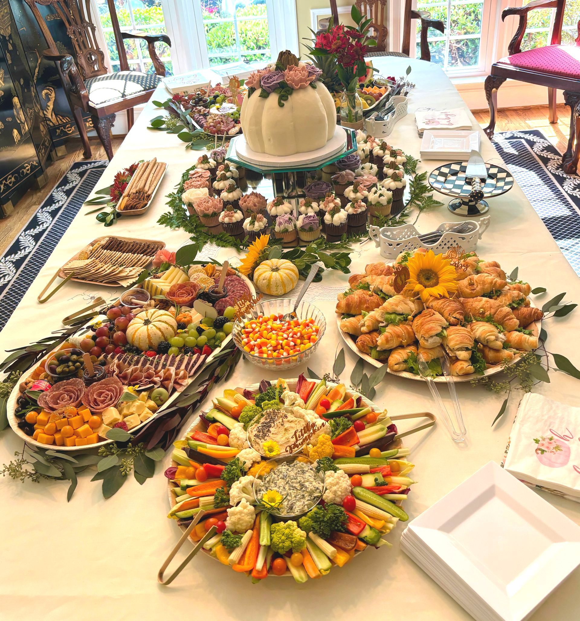 Long table with food platters, charcuterie, and pumpkin cake, set for a gathering.