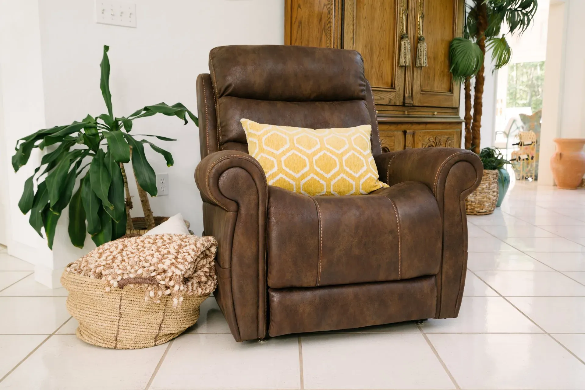 A brown recliner with a yellow pillow is sitting in a living room next to a plant.