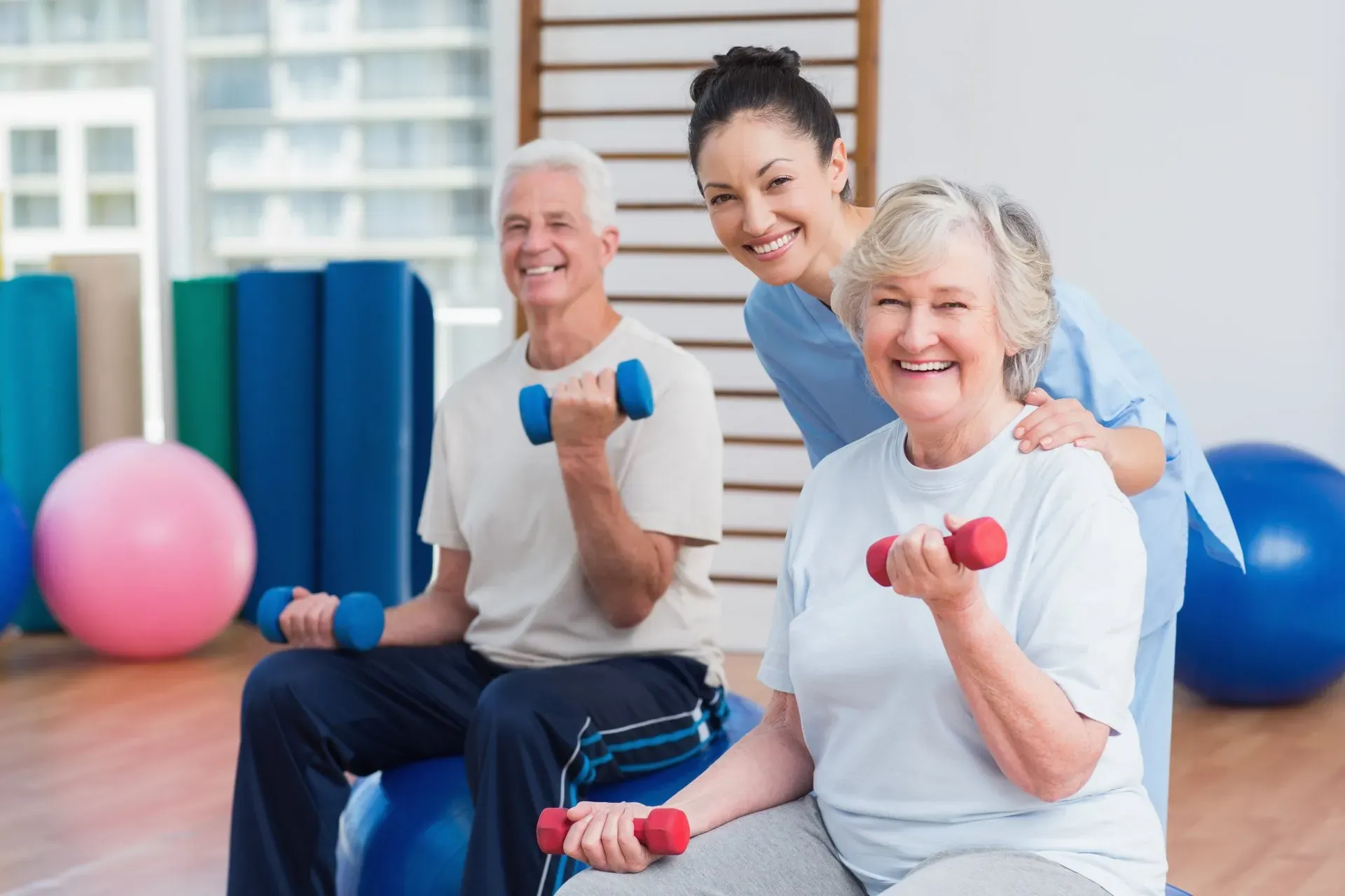 A nurse is helping two elderly people lift dumbbells in a gym.