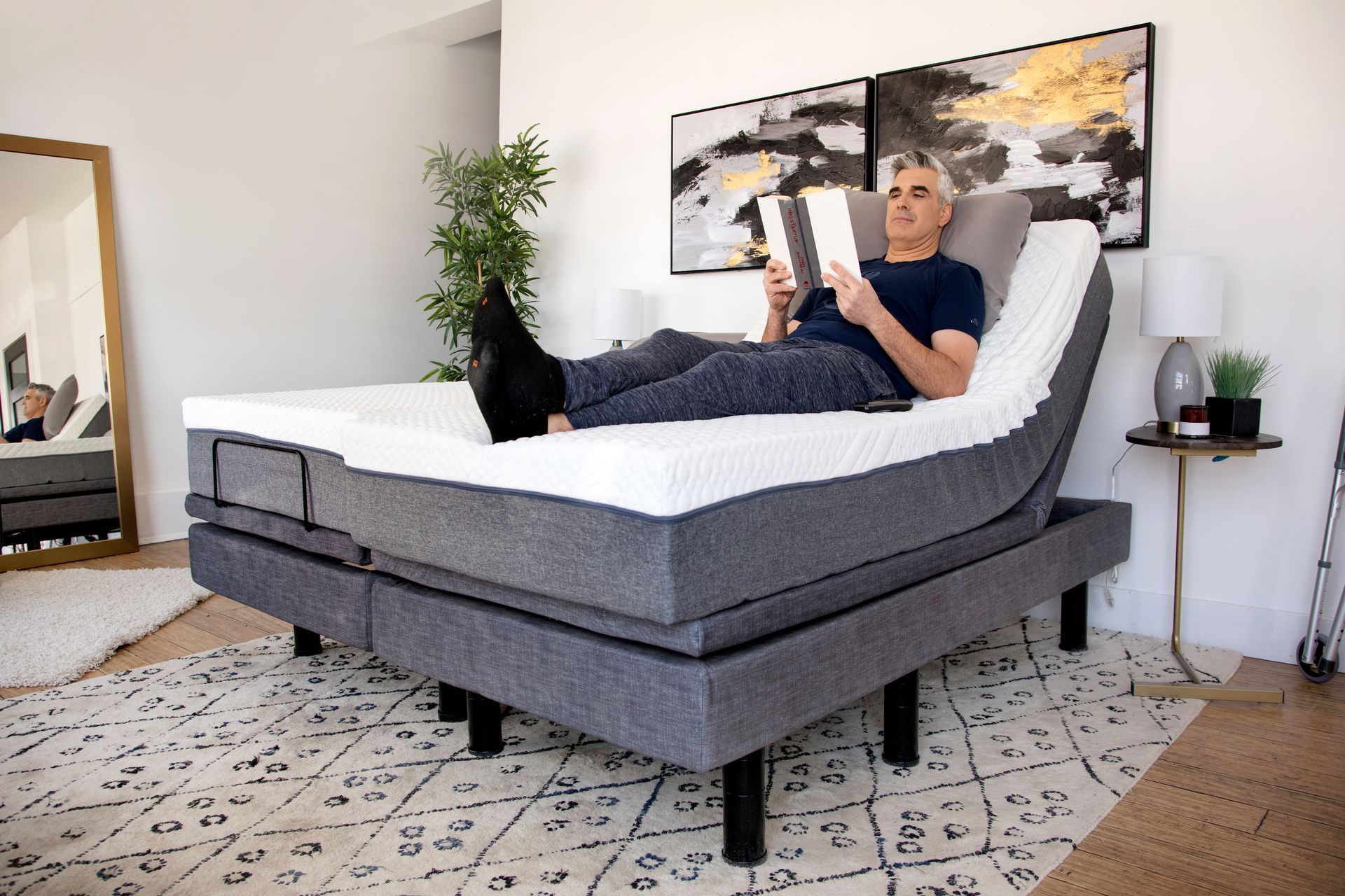 A man is laying on an adjustable bed reading a book.