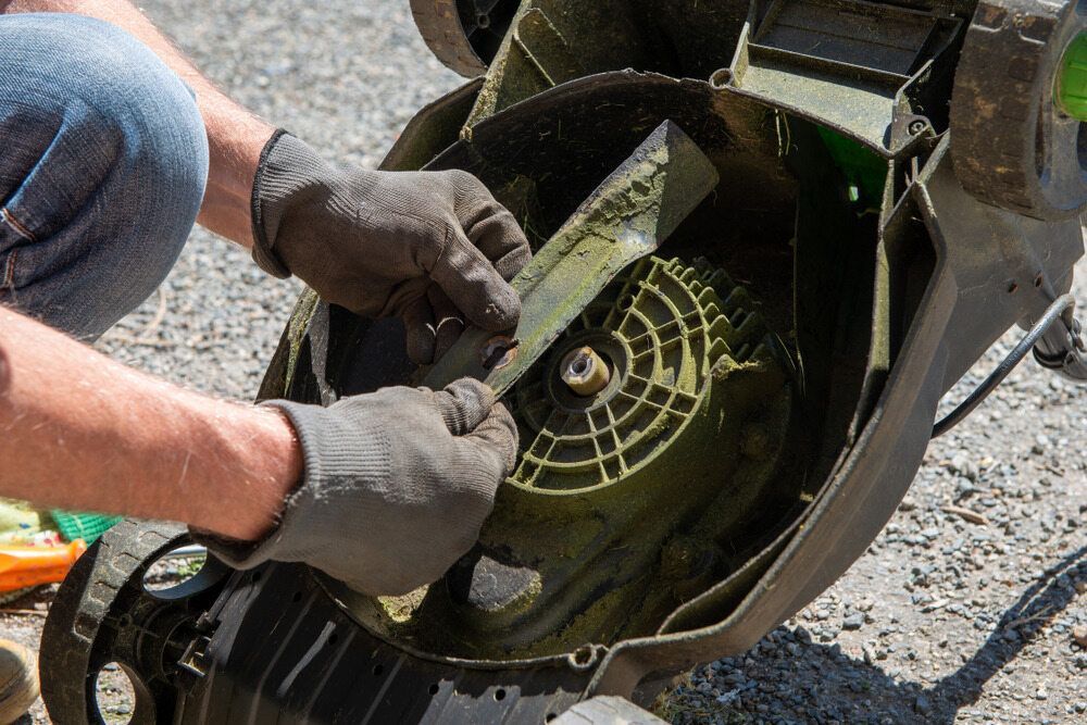 A Man Is Cleaning The Blades Of A Lawn Mower — Harry's Mower Repairs In Bundaberg North, QLD