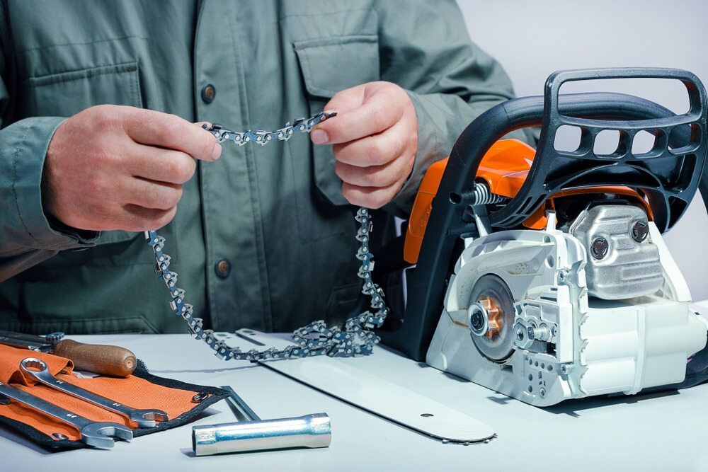 A Man Is Fixing A Chainsaw On A Table — Harry's Mower Repairs In Bundaberg North, QLD