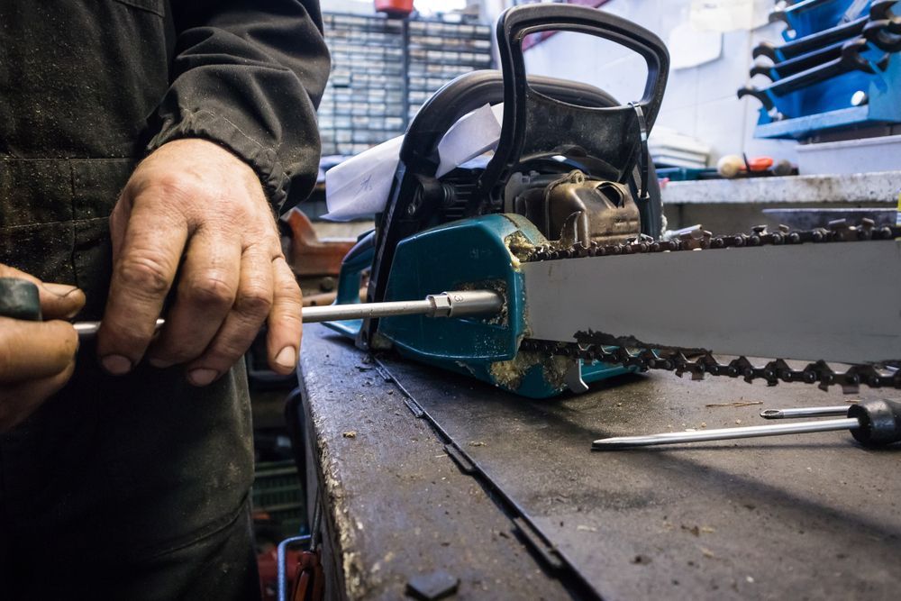 A Man Is Fixing A Chainsaw With A Screwdriver — Harry's Mower Repairs In Bundaberg North, QLD