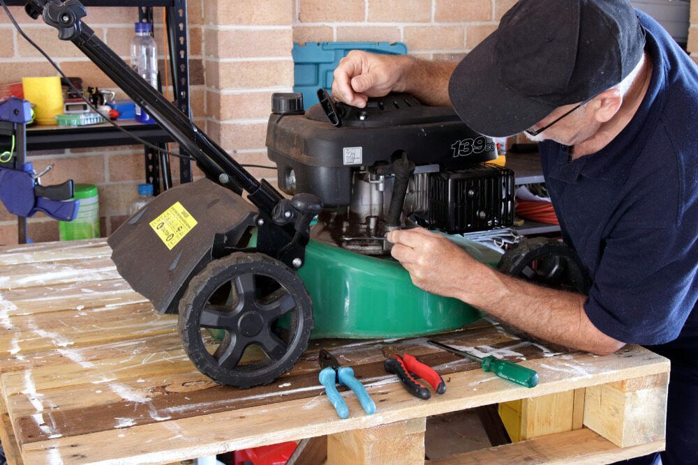 A Man Is Fixing A Lawn Mower On A Wooden Pallet — Harry's Mower Repairs In Bundaberg North, QLD