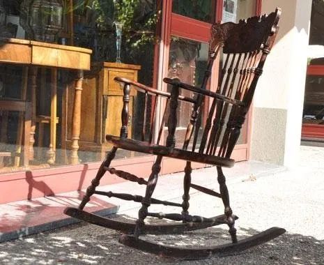 Una sedia a dondolo di legno è posizionata davanti alla vetrina di un negozio.