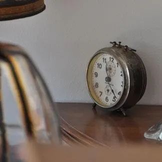 Una vecchia sveglia è appoggiata su un tavolo di legno accanto a una lampada.