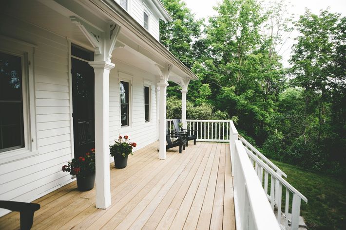 A white house with a large porch with chairs and flowers on it A white house with a large porch with chairs and flowers on it