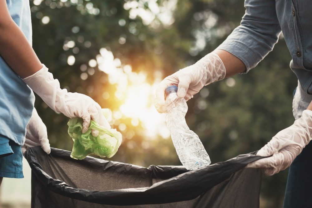 Man And A Woman Throwing Plastic Bottles Into A Trash Bag — Kanga Bins Qld Pty Ltd In Mulara, QLD