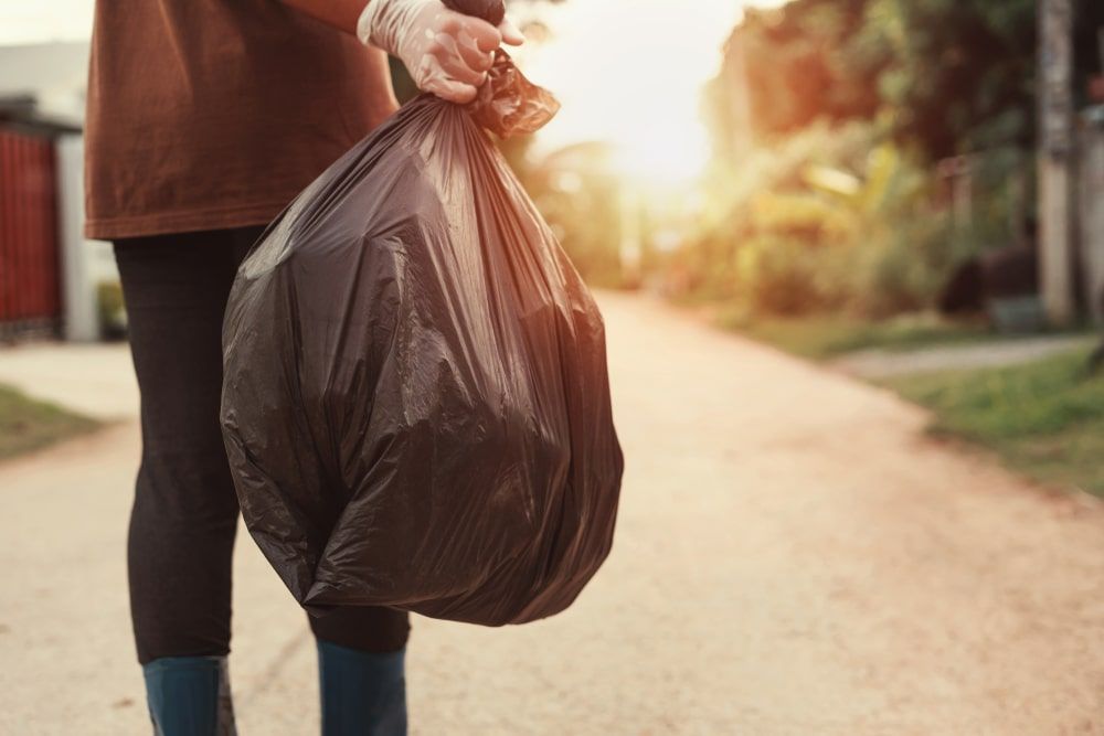 Woman Carrying A Trash Bag On A Dirt Road — Kanga Bins Qld Pty Ltd In Mulara, QLD