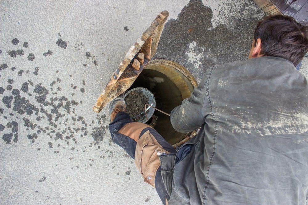 Man Cleaning A Manhole With Open Cover Using A Bucket — Kanga Bins Qld Pty Ltd In Mulara, QLD