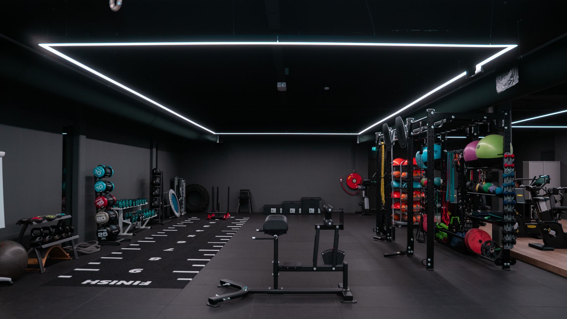 Interieur van sportschool met fitnessapparaten, zwarte muren en plafondverlichting.