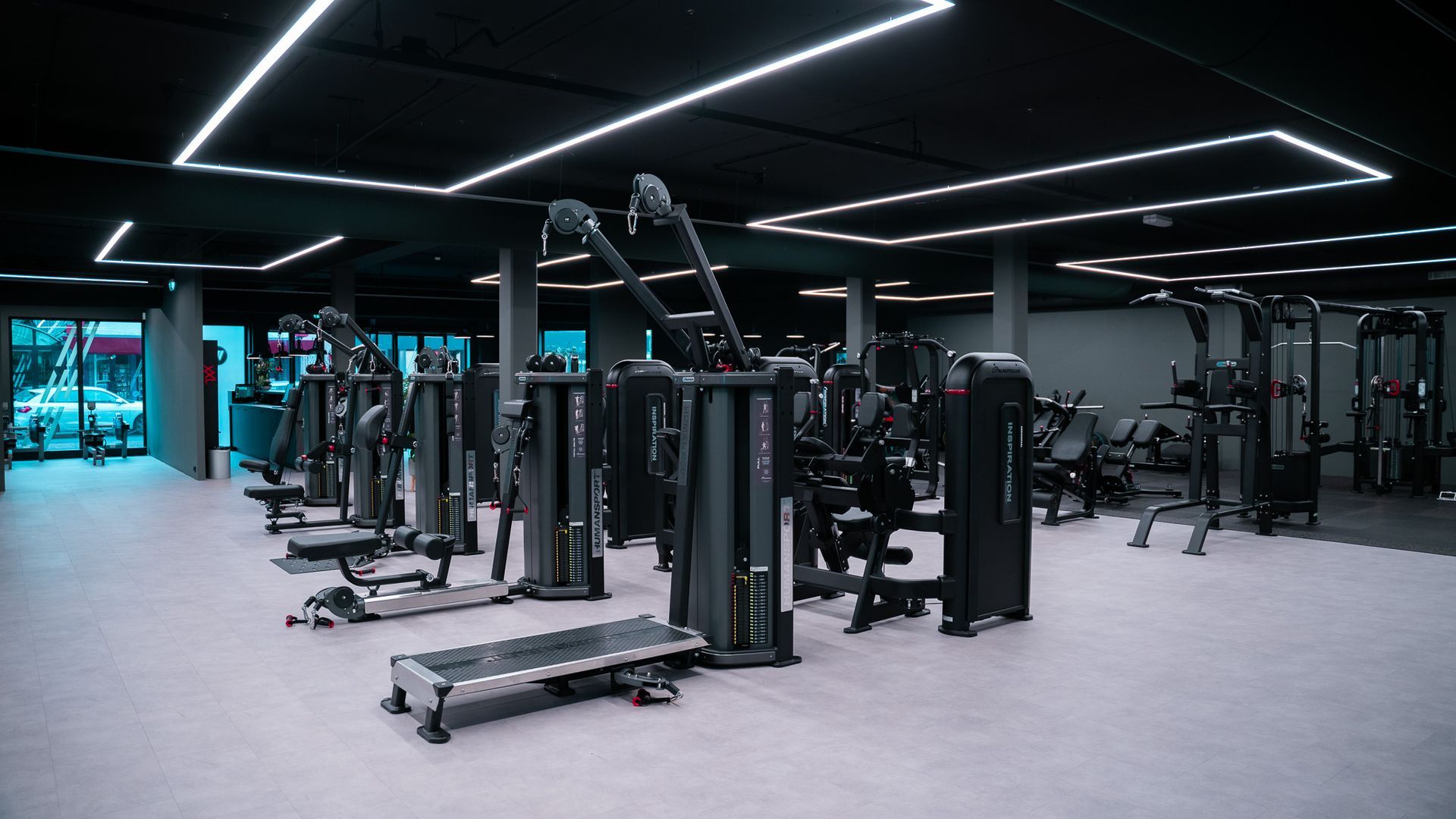 Sportschoolinterieur met diverse fitnessapparaten, verlicht door plafondlampen.