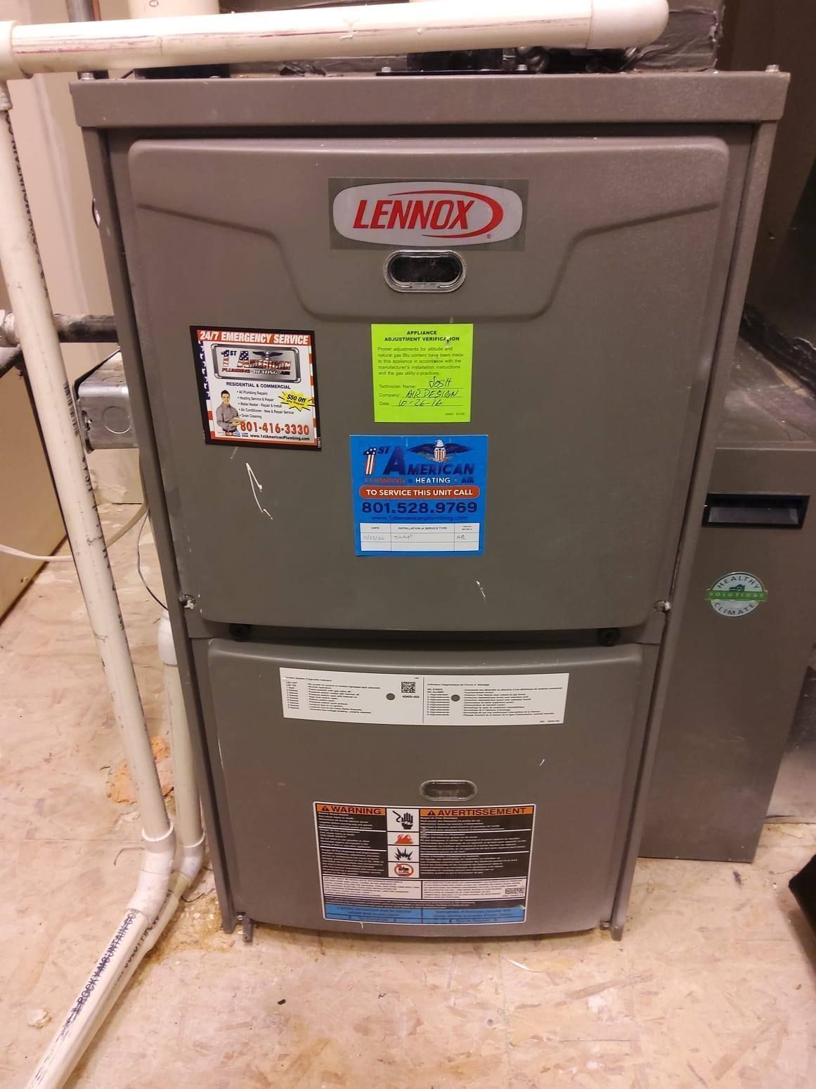 Lennox furnace unit in a basement setting. Gray metal with stickers. White pipes and concrete floor.