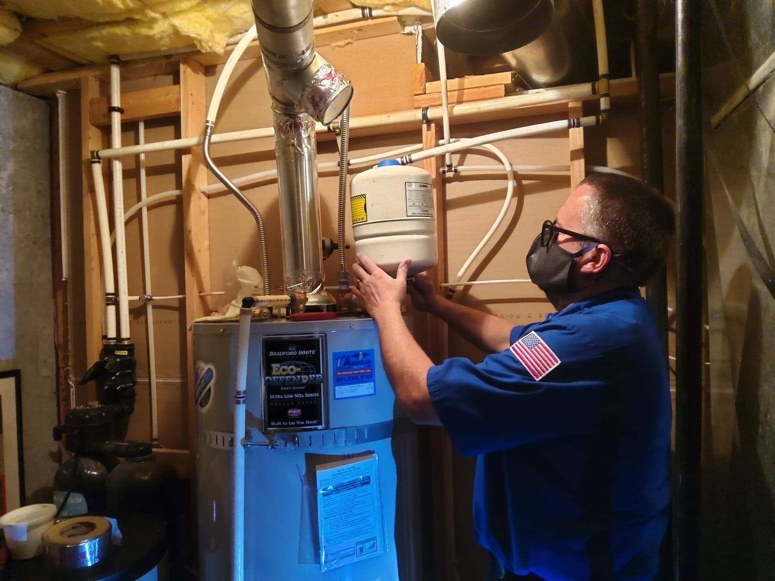 Person in a blue shirt and mask working on a water heater, indoors.