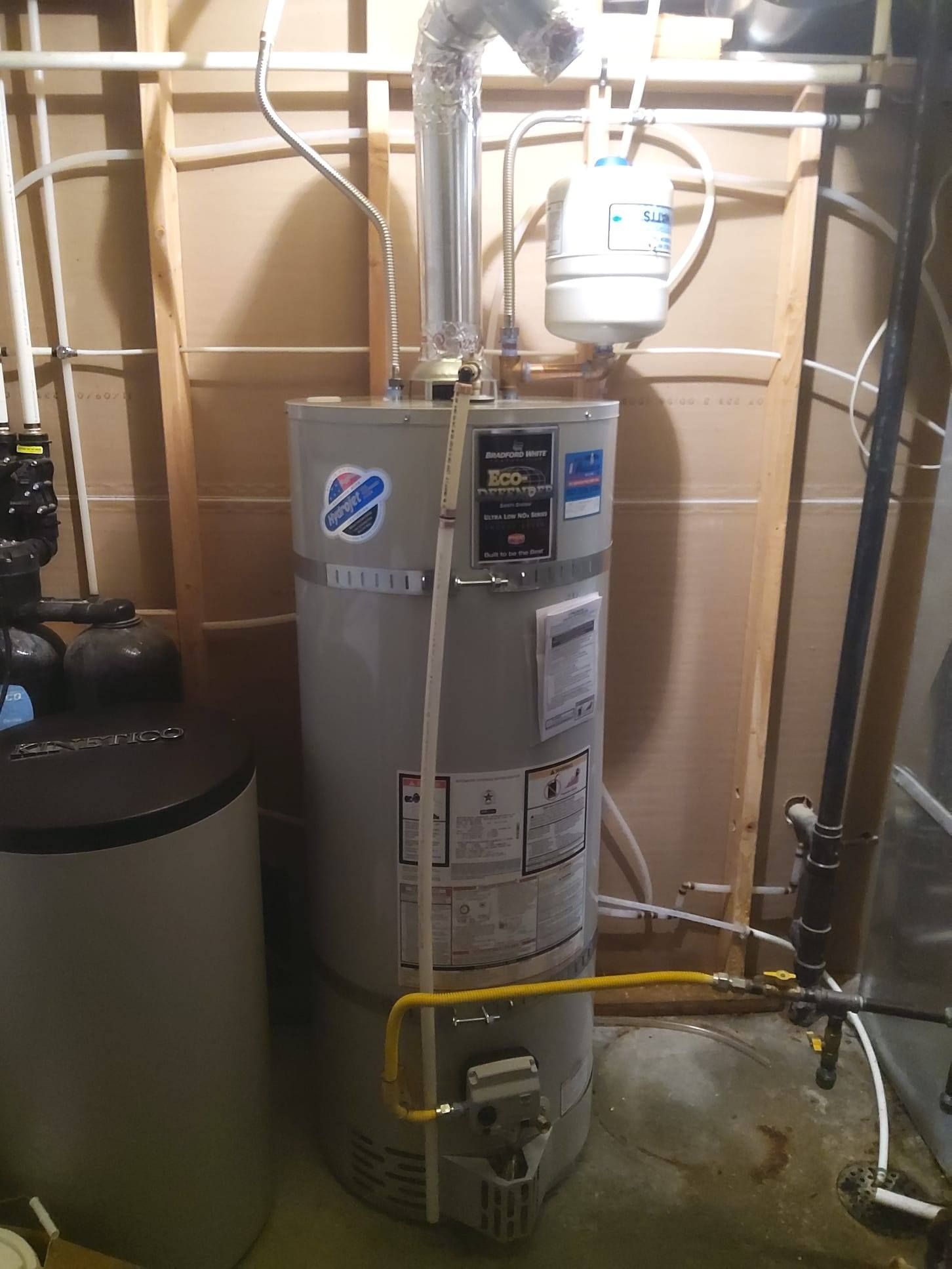 Water heater in a basement setting. Gray tank with silver flue, gas line visible.
