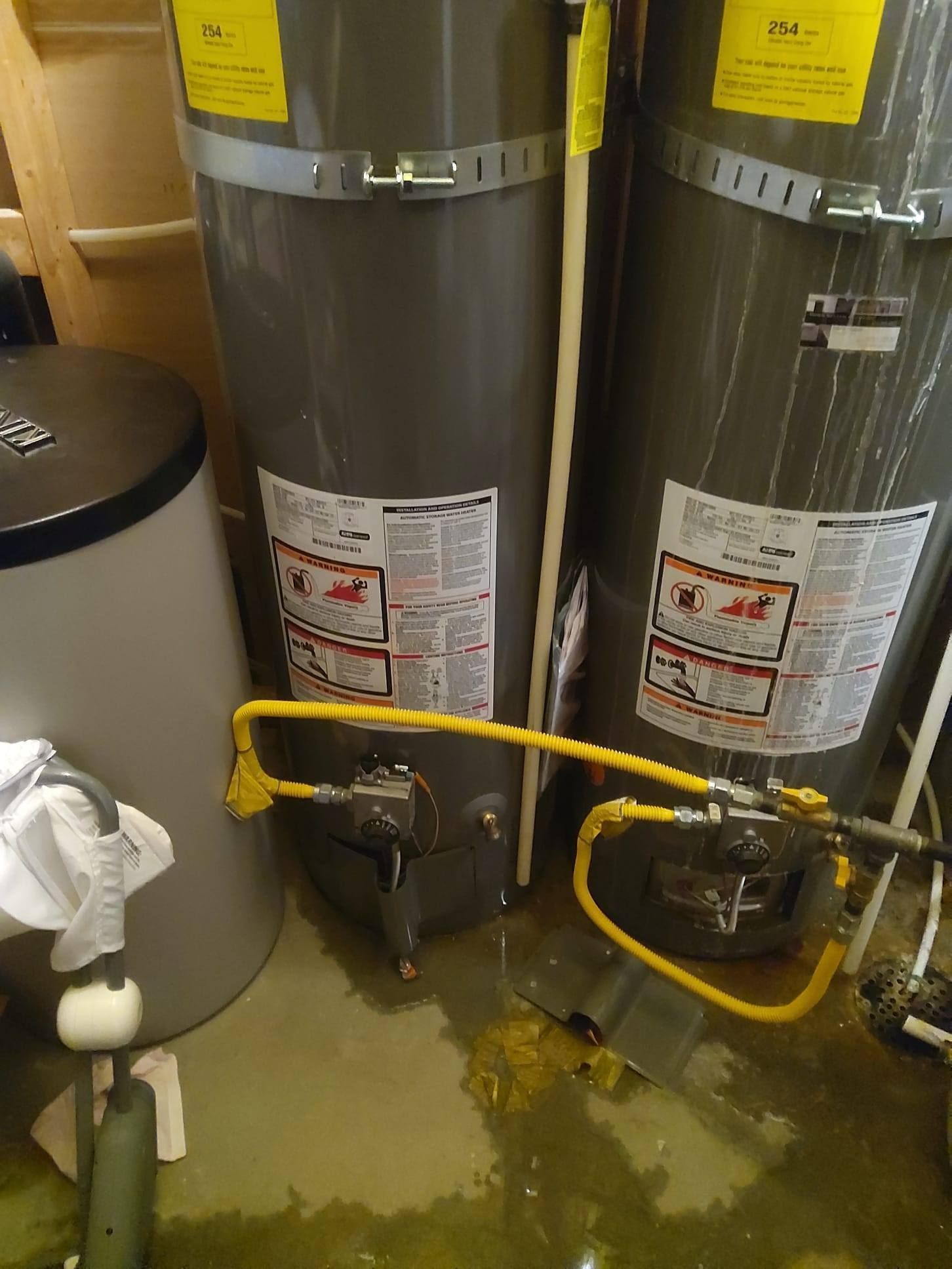 Two gray water heaters with yellow gas lines are in a flooded basement.