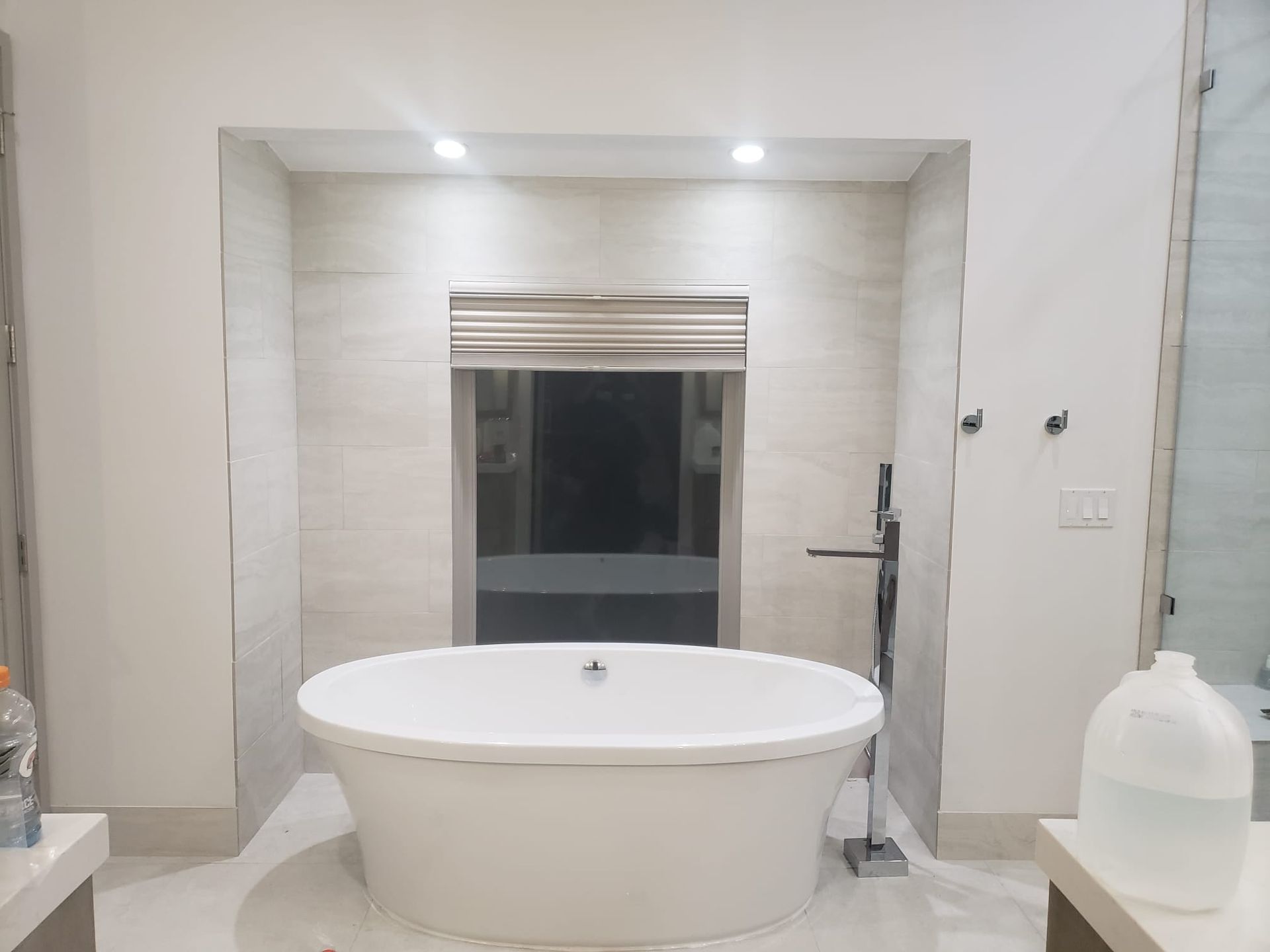 White oval bathtub in alcove with a window, tile, and two spotlights.
