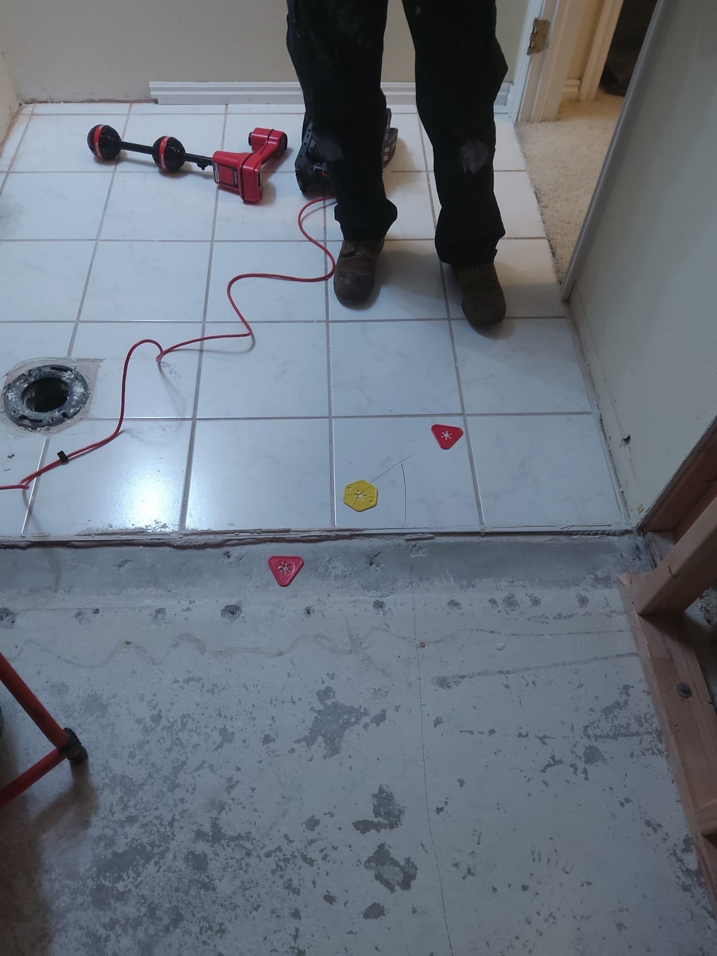 Person standing on white tiled floor in a bathroom under construction. Red and yellow markers are present.