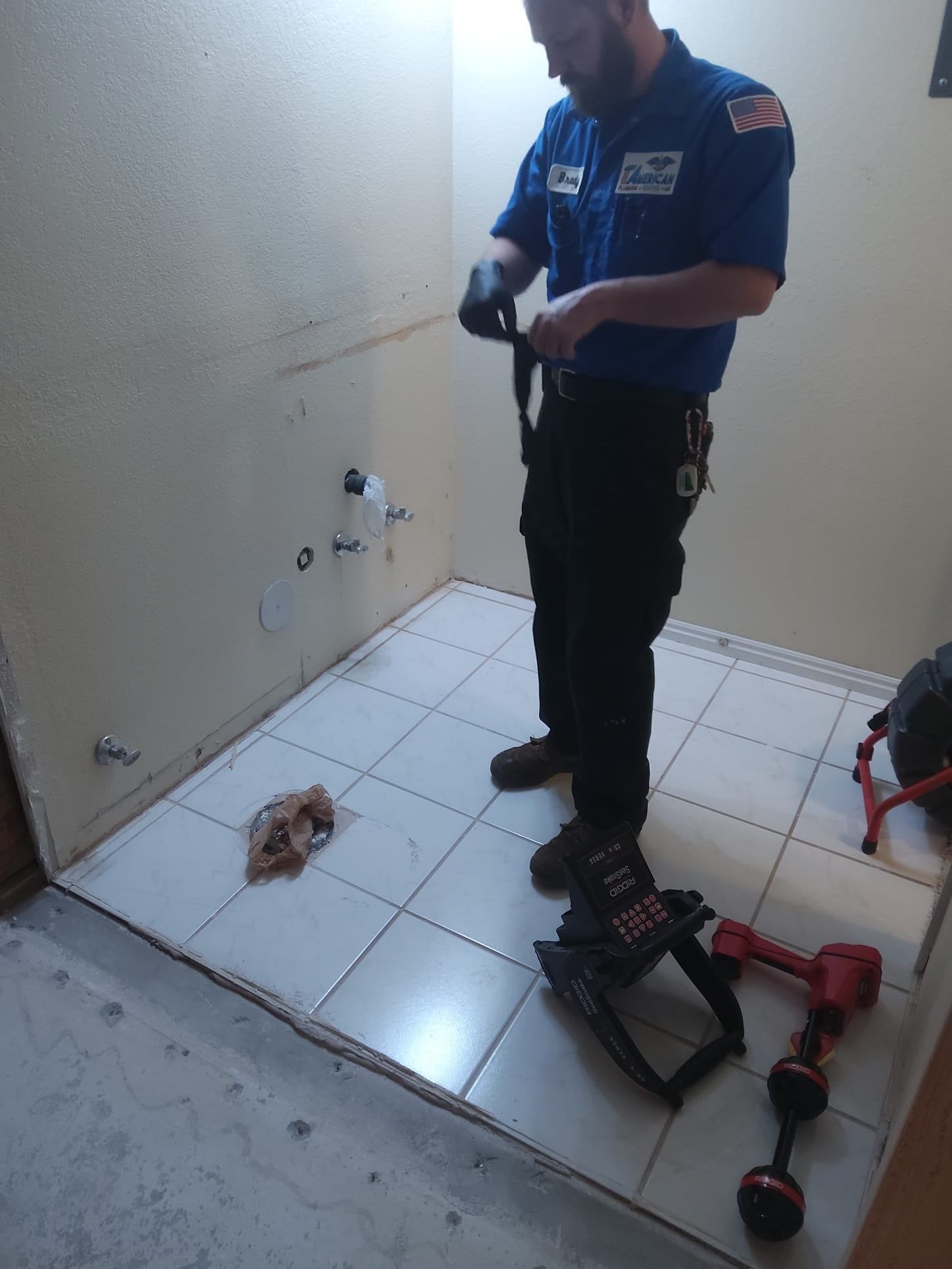 Plumber in blue uniform prepares tools in a tiled bathroom.
