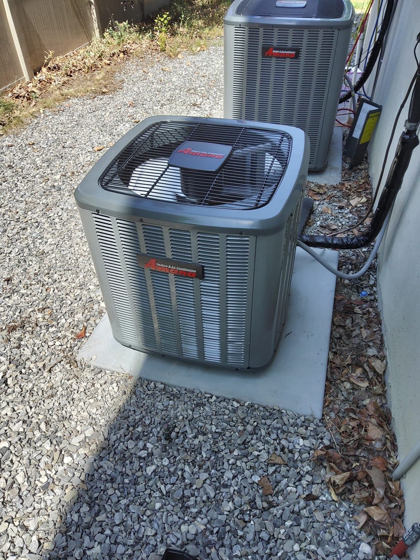 Two gray HVAC units outdoors on concrete pads, surrounded by gravel.