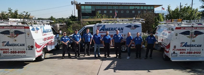 Group of technicians in blue shirts stand in front of three service vans. Buildings and trees are in the background.