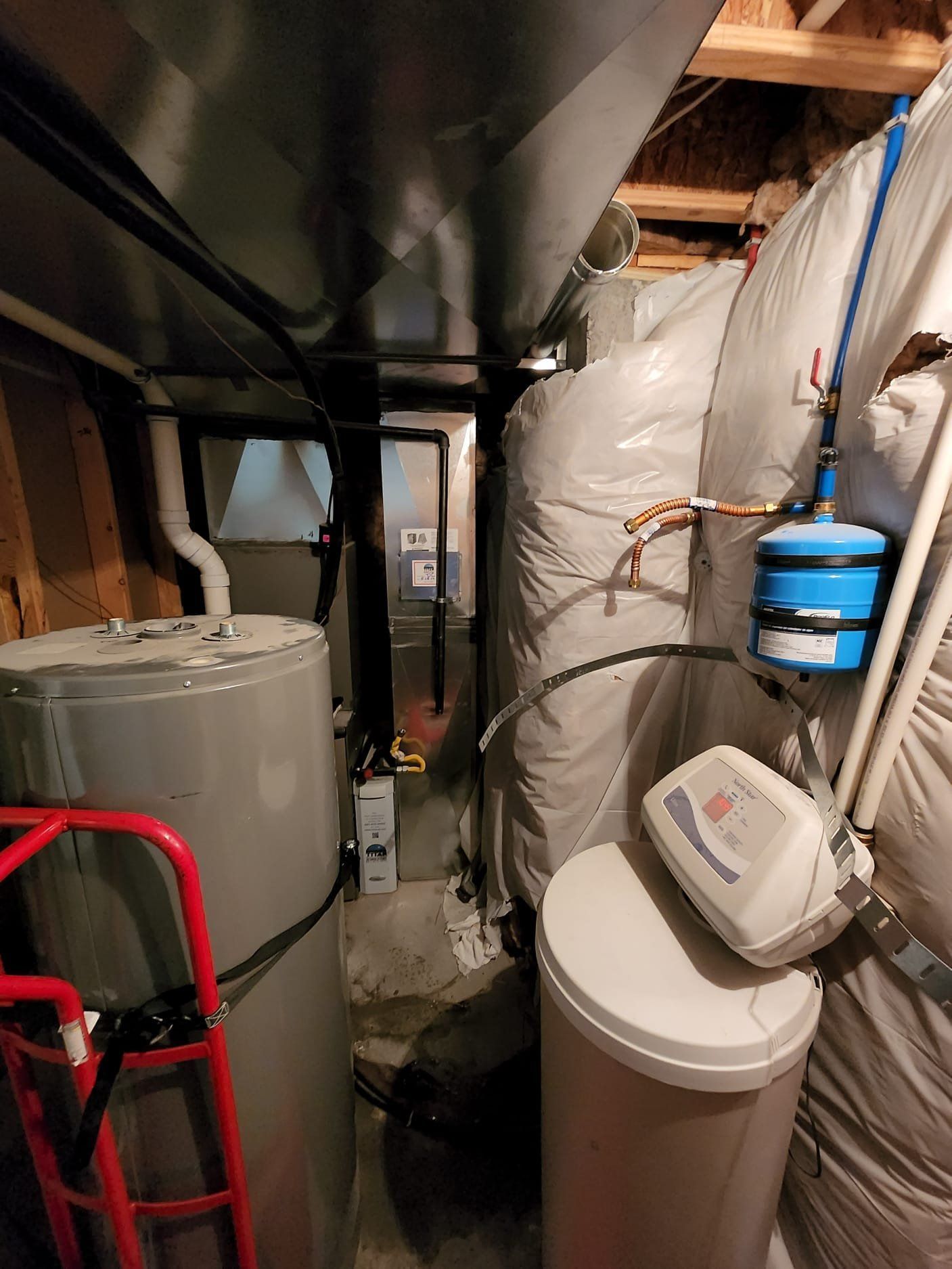Basement with water heater, water softener, and ductwork. Red step ladder leans against water heater.