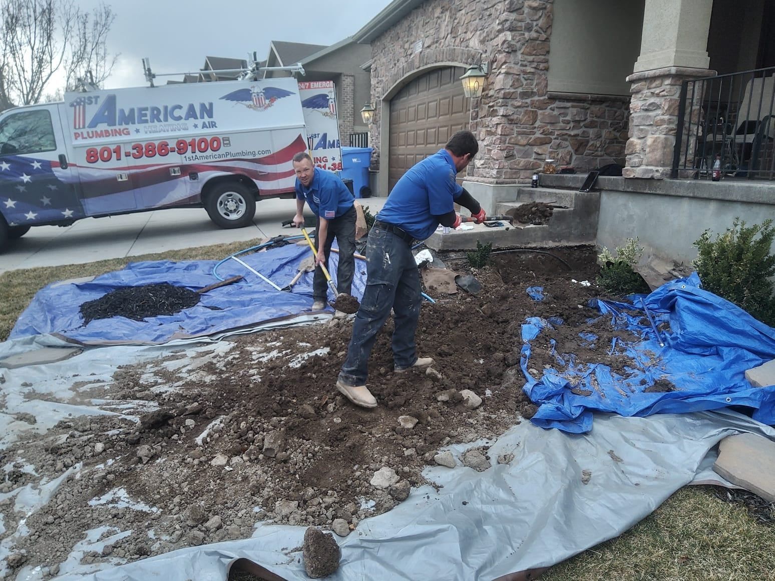Two workers digging in a yard near a house with an American Plumbing truck in the background. Blue tarps on the ground.