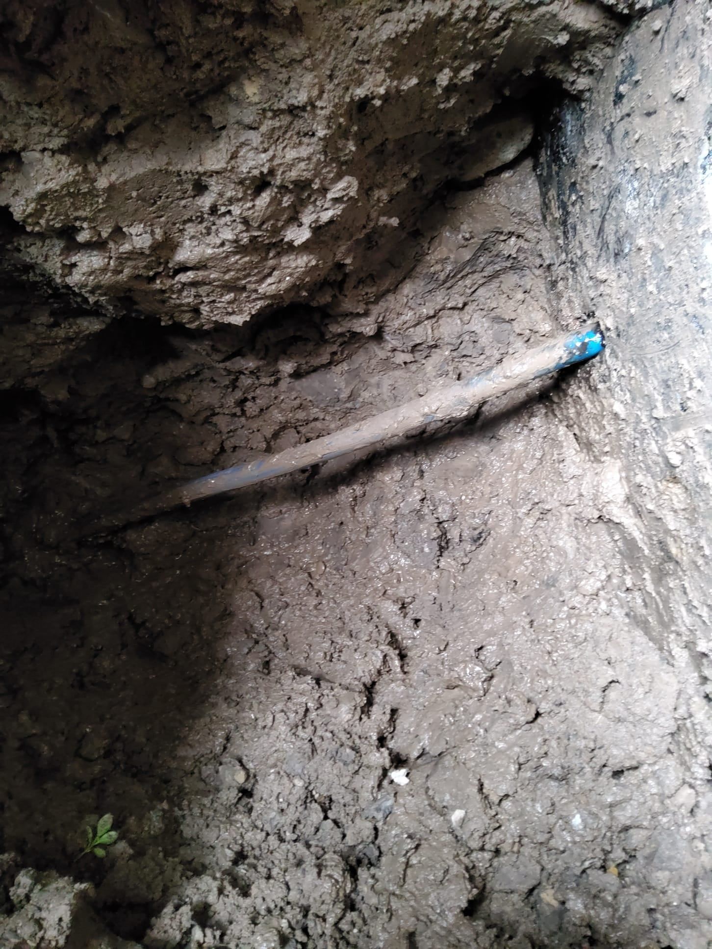A buried pipe in a dirt trench; one end has a blue cap.