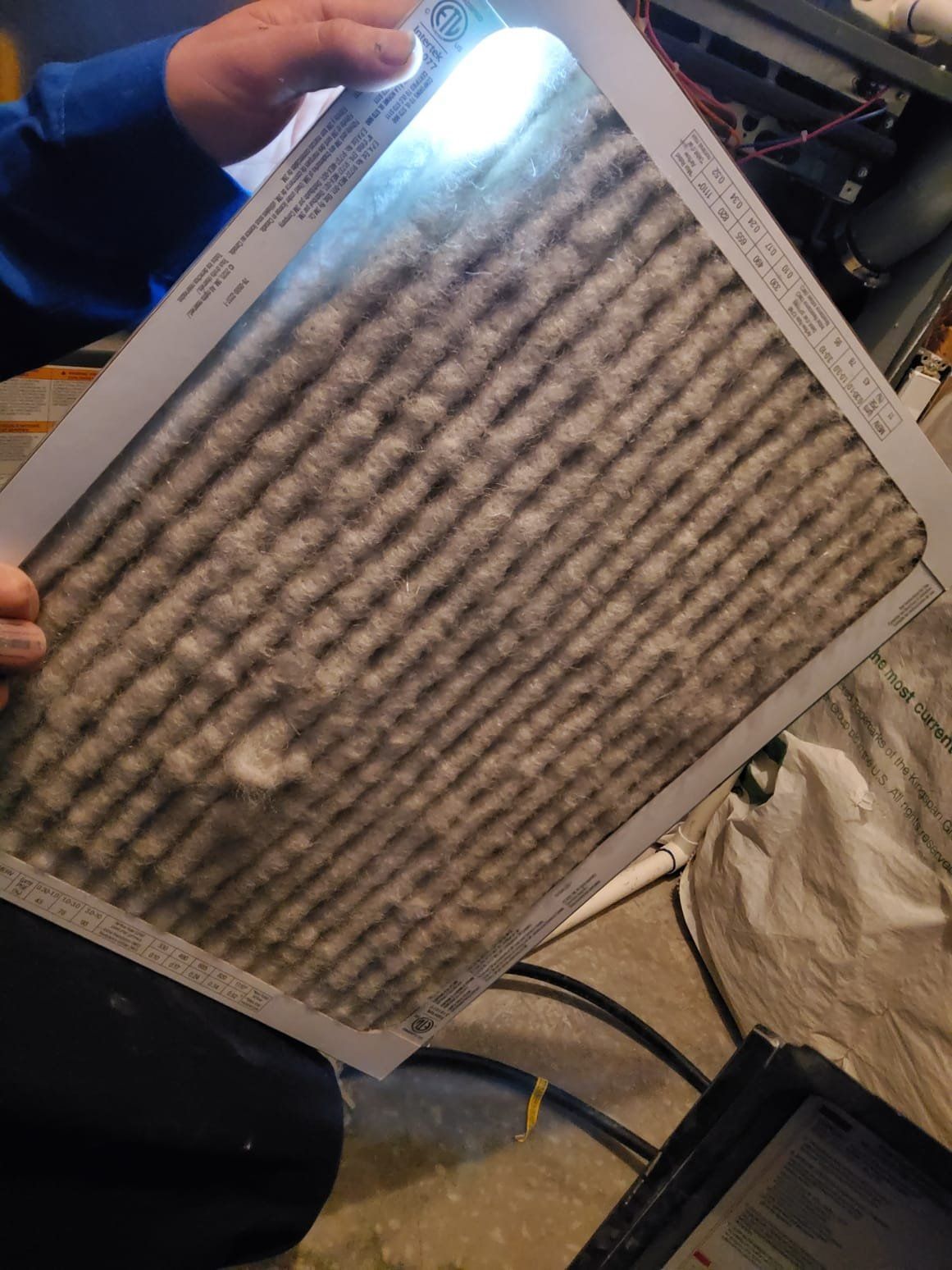 Dirty HVAC filter held up, illuminated by a light.