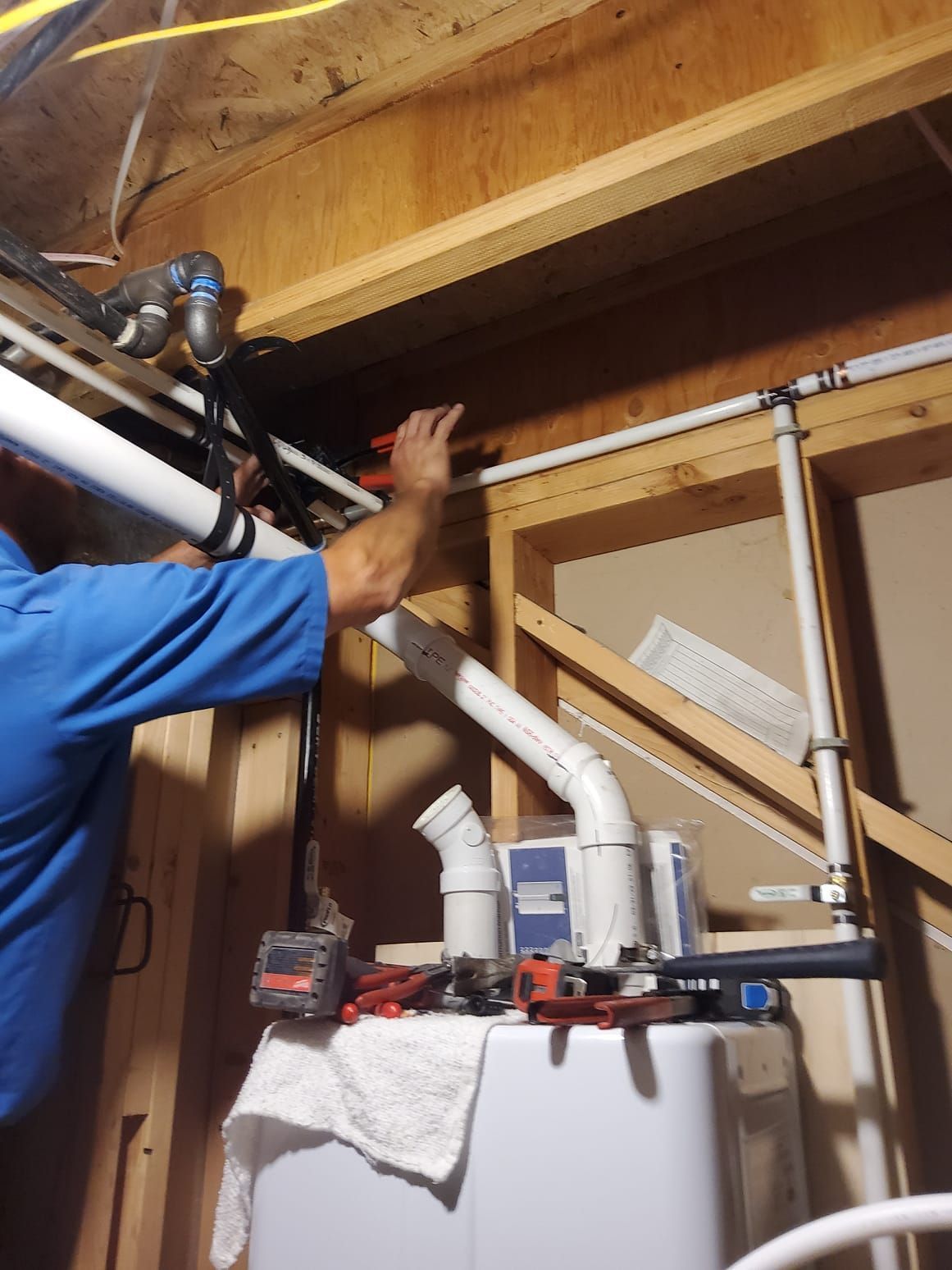 Person working on plumbing, using a wrench. White pipes, water heater, in a basement.
