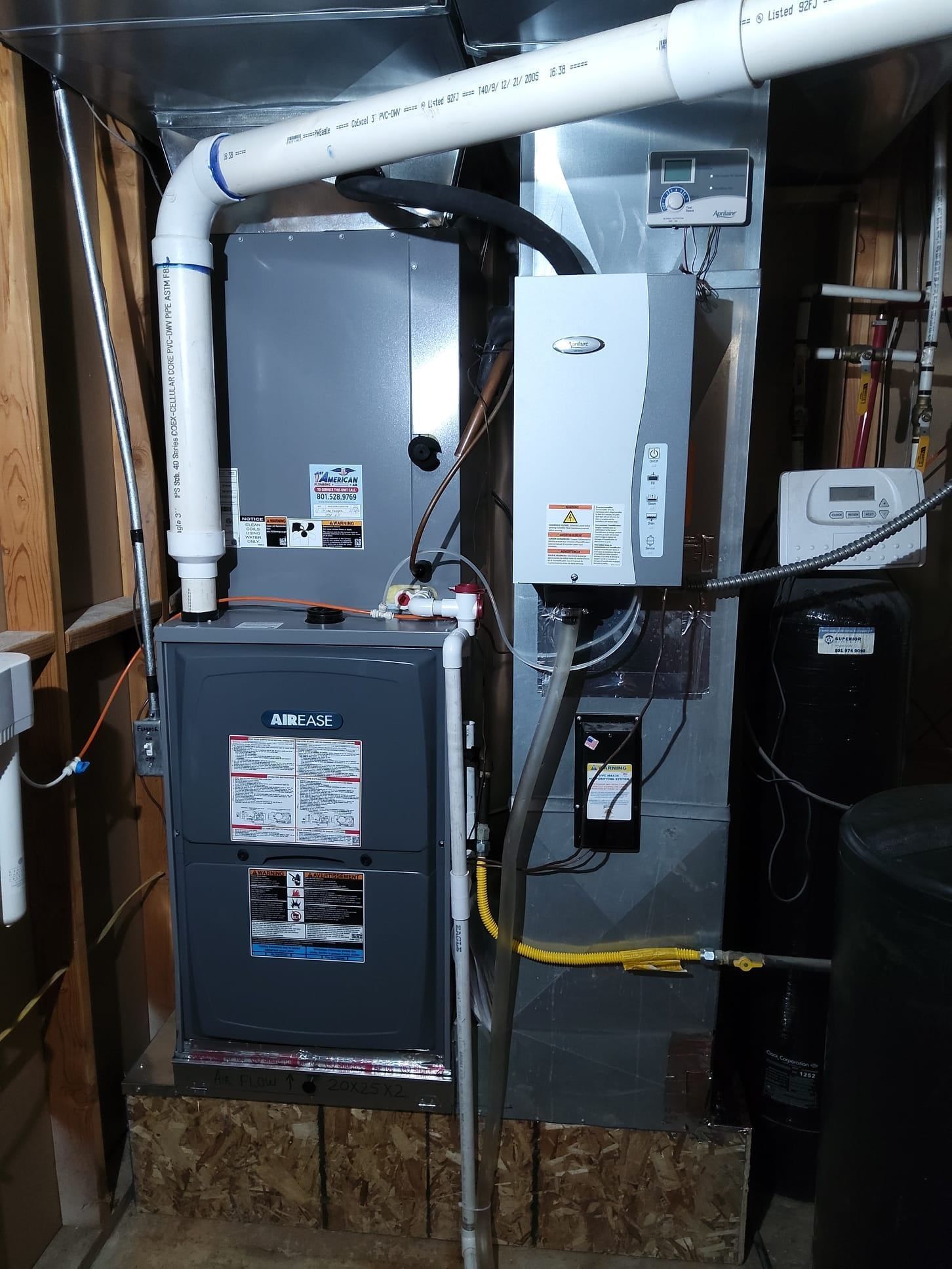 Furnace and water heater in a basement. Metal units with pipes, ductwork, and electrical wiring.