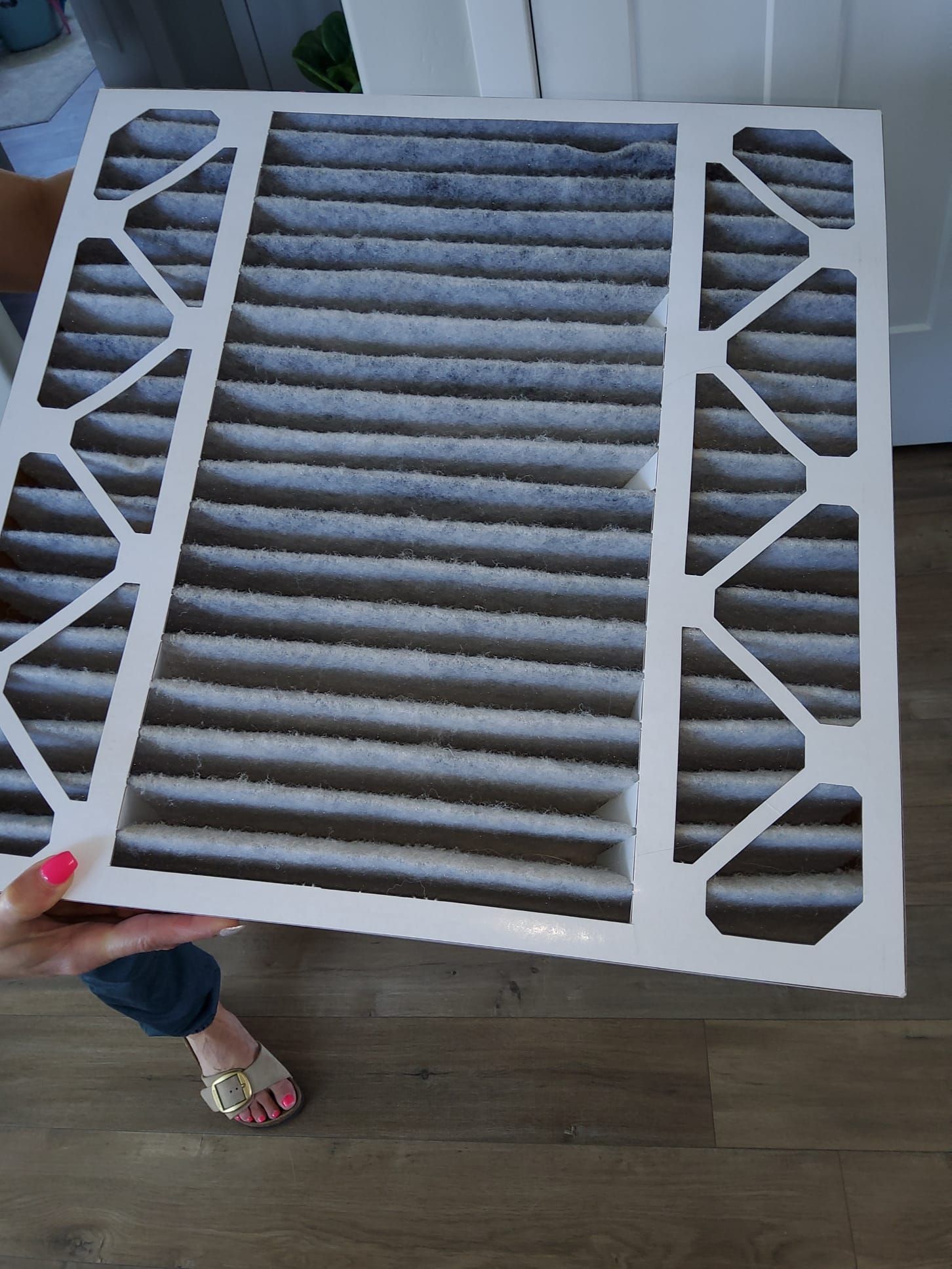 Dirty air filter held by a person indoors. Filter is clogged with dust.