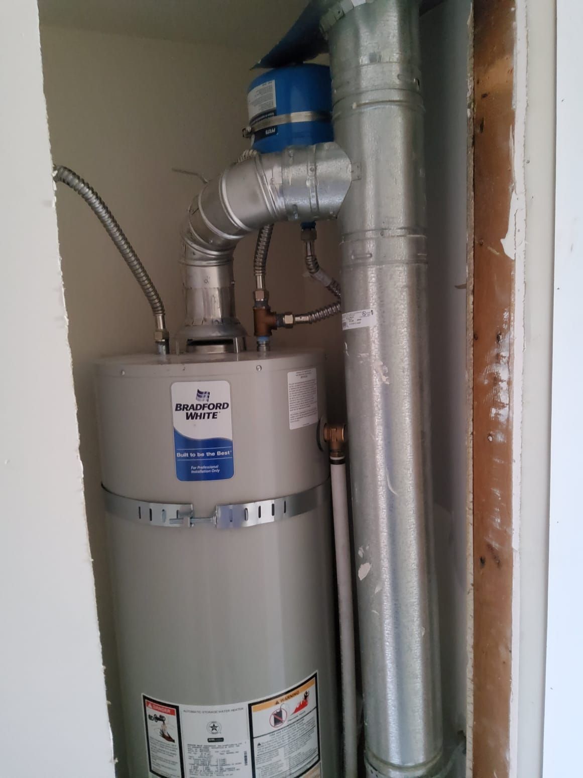 A gas water heater in a utility closet with vent pipes and flexible gas line.
