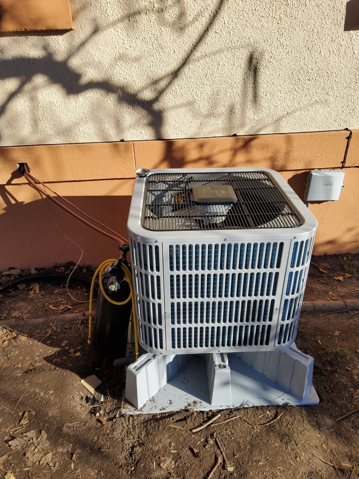 An outdoor air conditioning unit with a metal cage, next to an exterior wall.